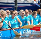 In einem großen Boot auf dem Wasser sitzen Menschen mit Paddeln und warten