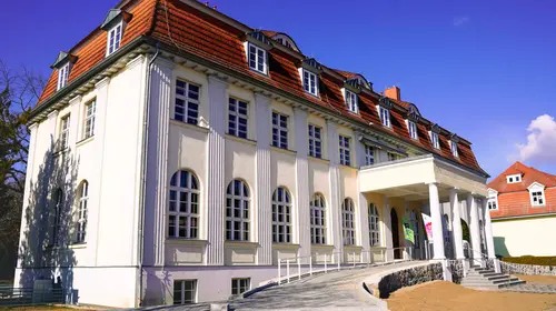 Eine ältere Villa mit drei Stockwerken, großem Einfahrtsbereich mit Säulen und überdachtem Eingang.